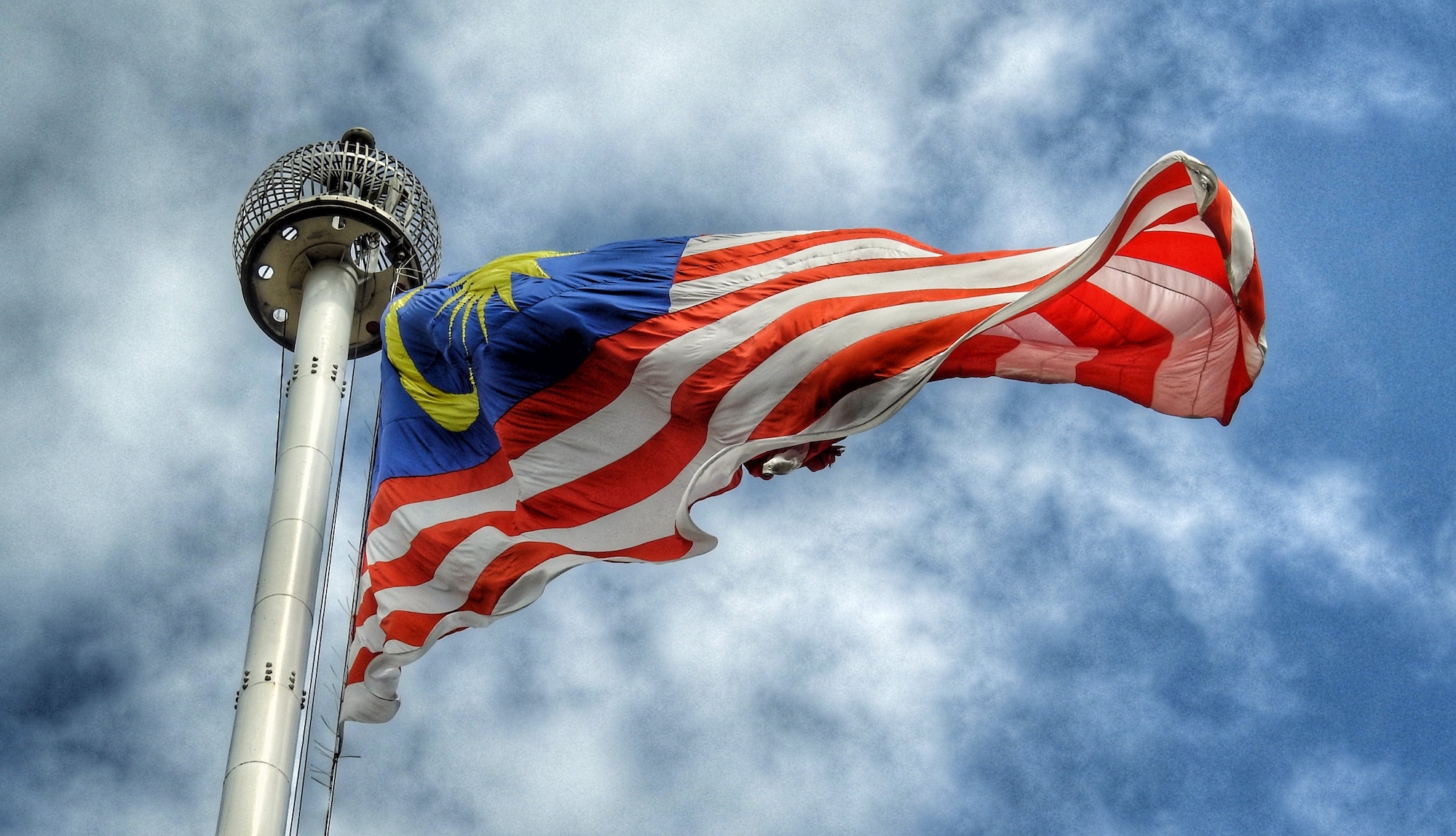 Malaysia flag blows with blue sky and clouds behind