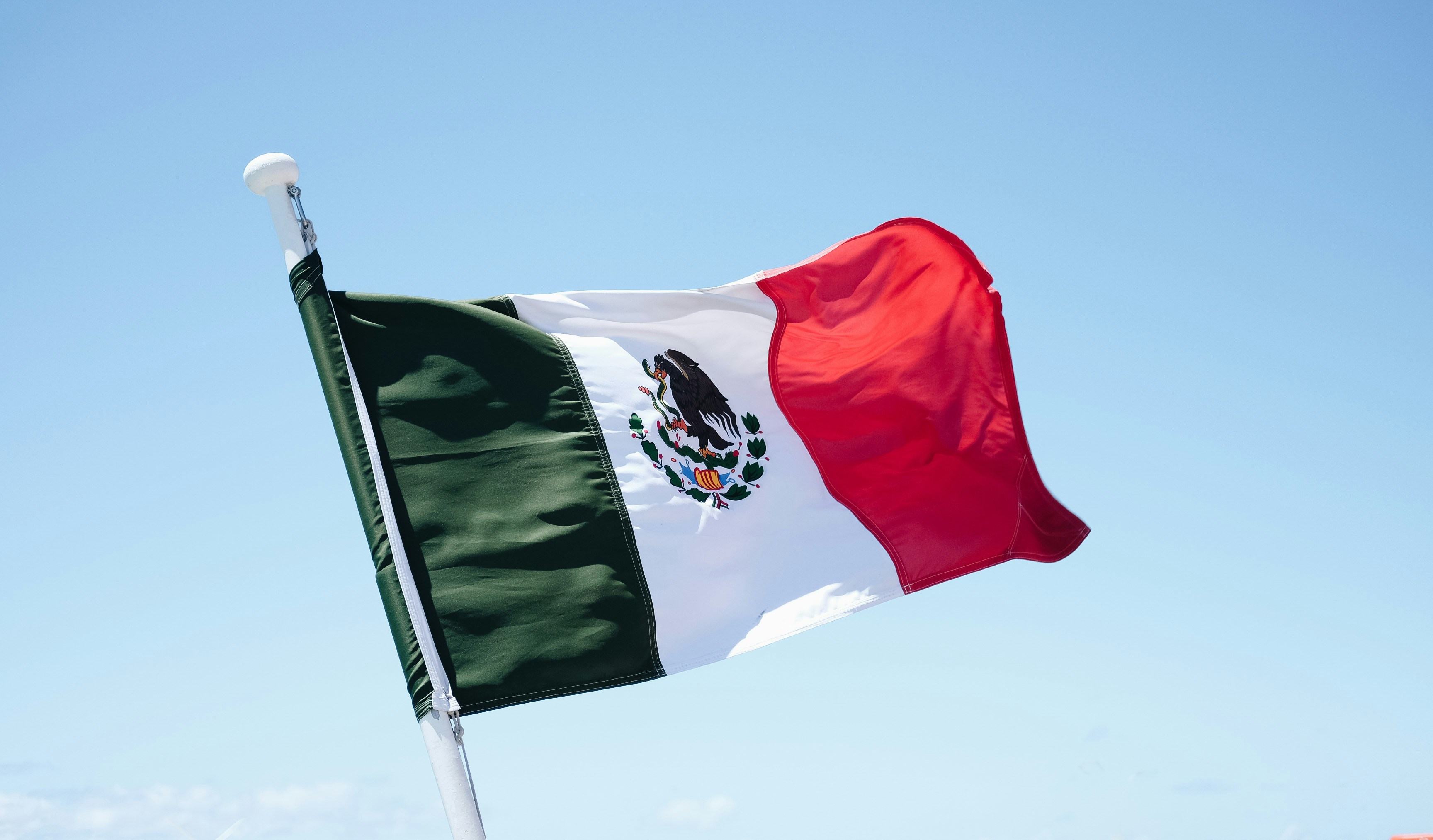 Photo of the Mexican flag blowing in the wind against a blue sky