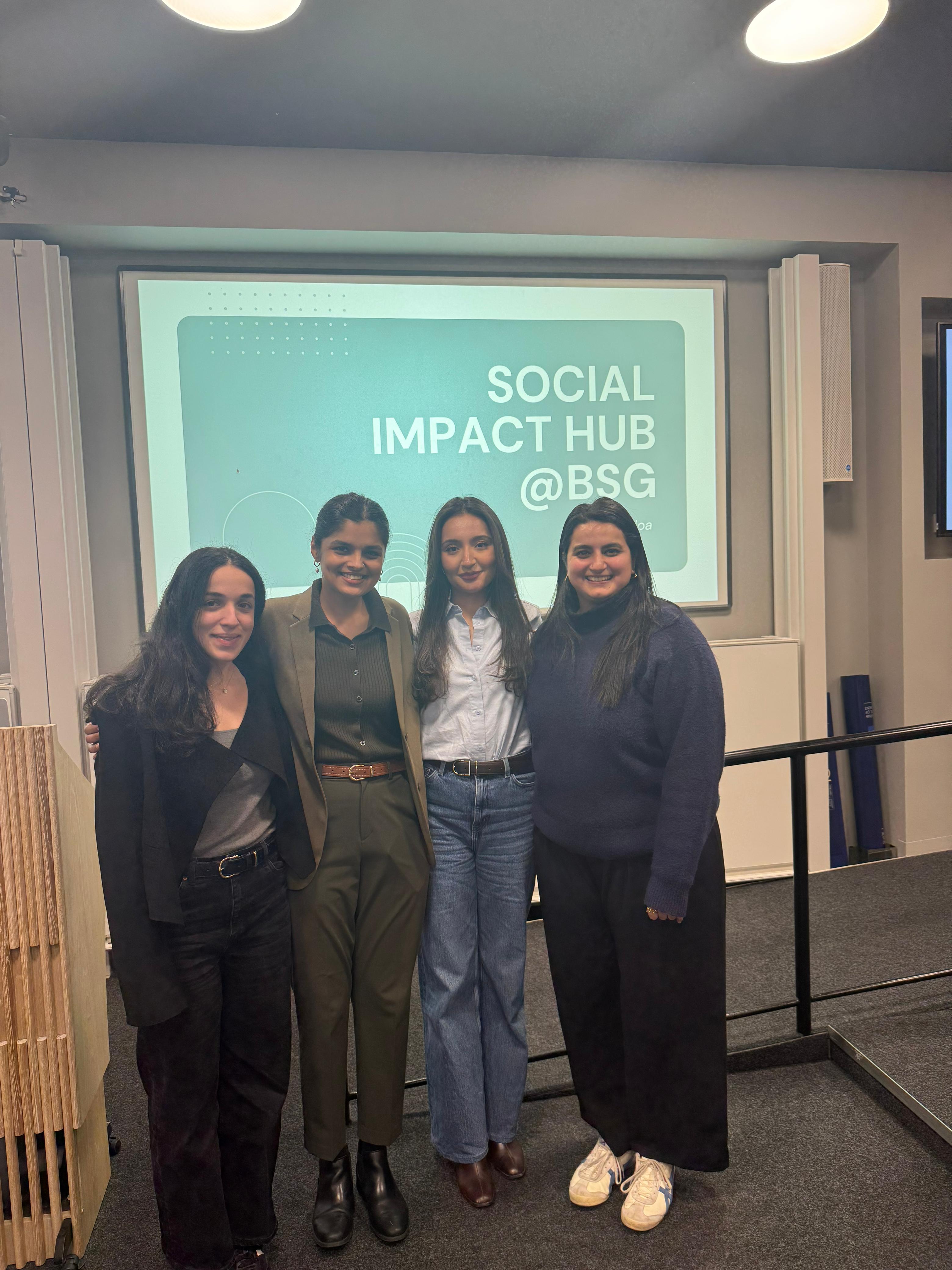 Group of students stand against a blue screen which says "social impact hub @ BSG"