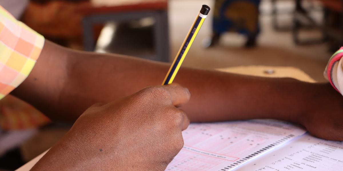 A close up of hand and an exam paper of the Basic Education Certificate Examinations in Ghana.