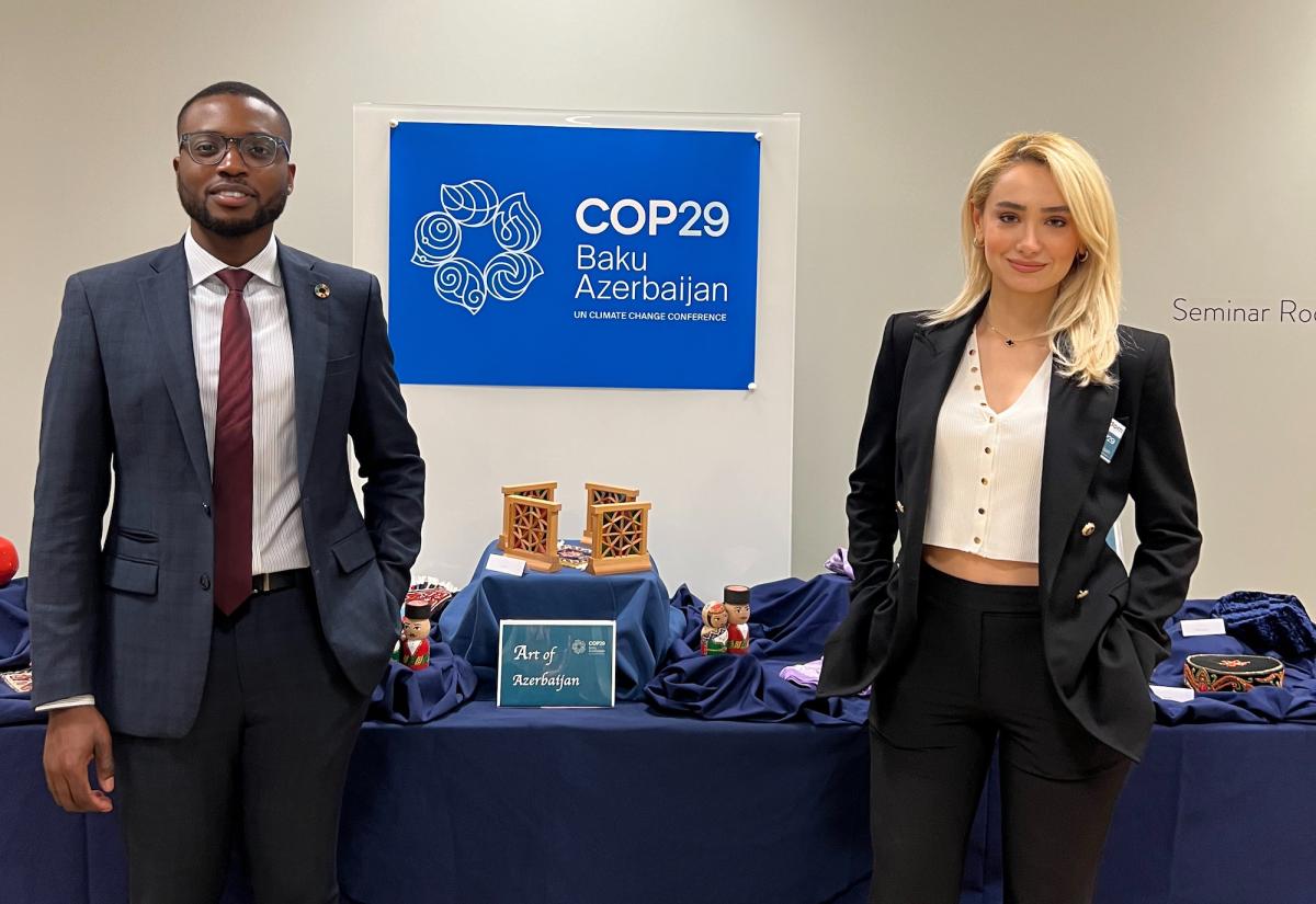 Kay Atanda and Laman in from of COP29 poster