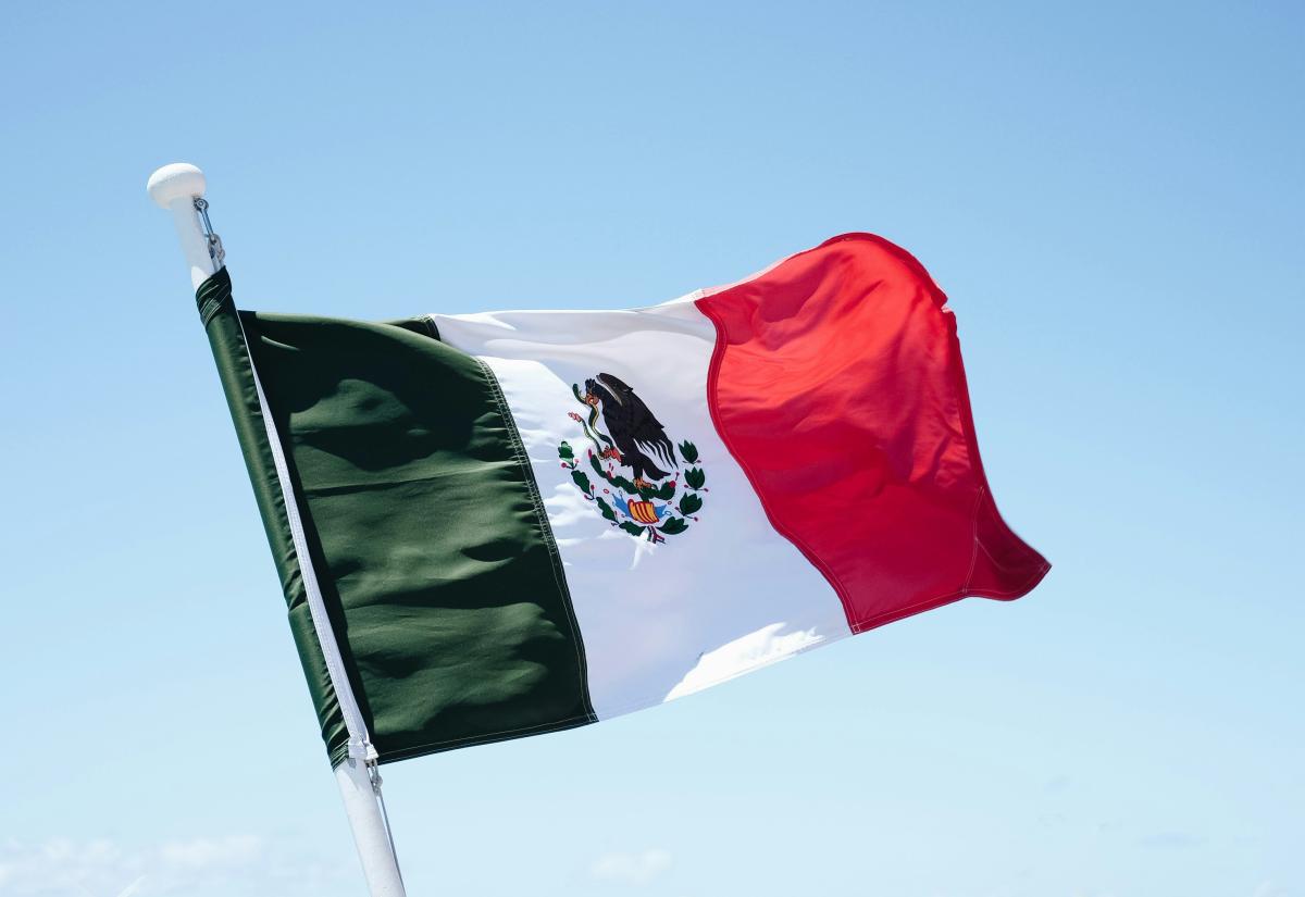 Photo of the Mexican flag blowing in the wind against a blue sky