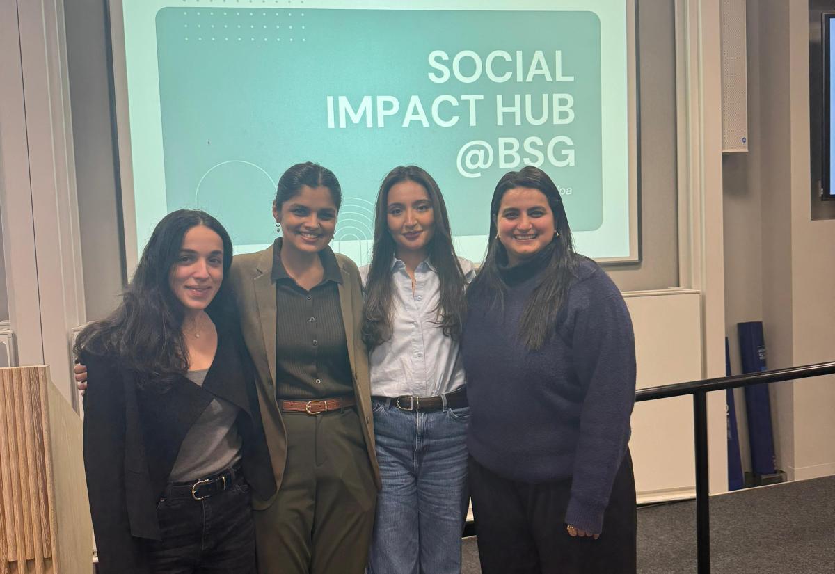 Group of students stand against a blue screen which says "social impact hub @ BSG"