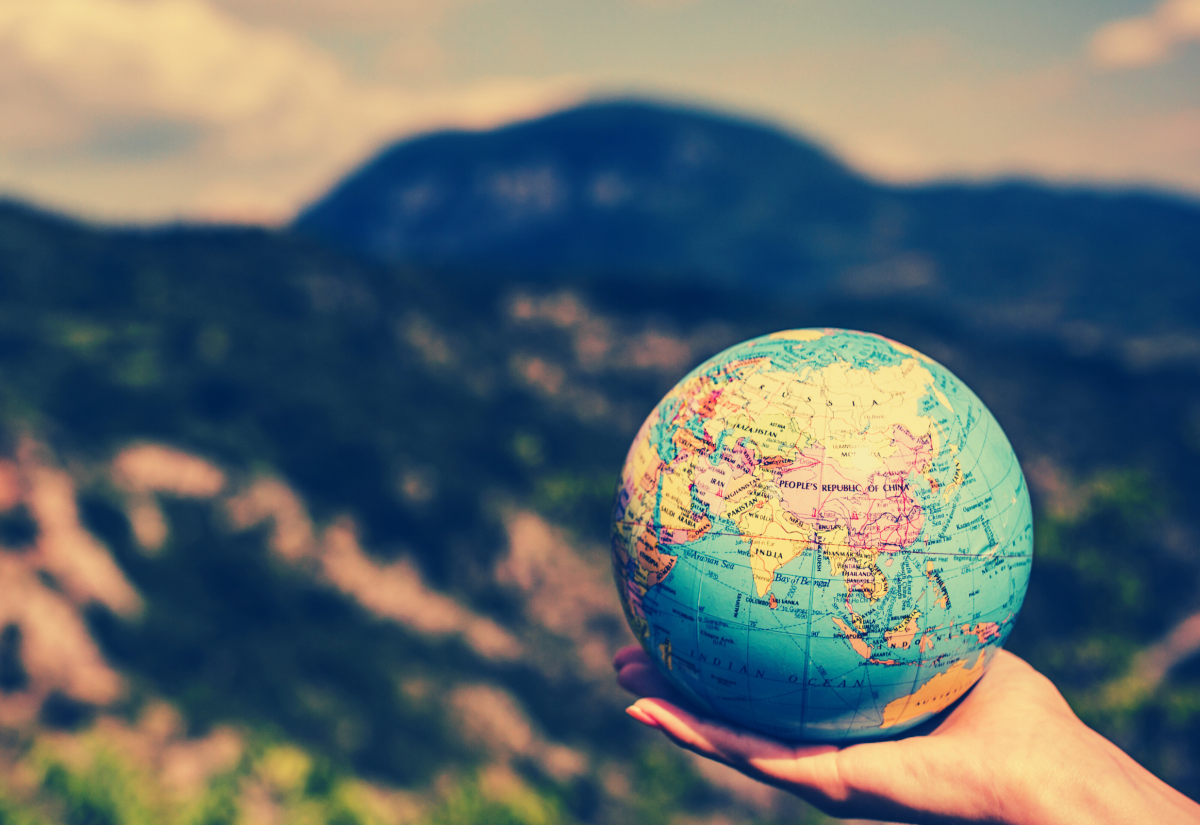 Globe held in hand against backdrop of mountains