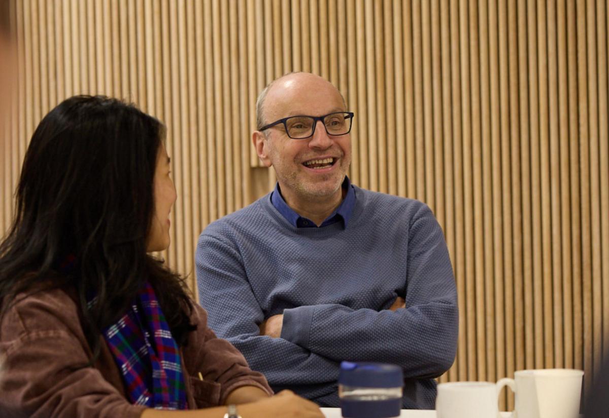 Professor Stefan Dercon sits at a table during induction next to two women. They are all smiling.